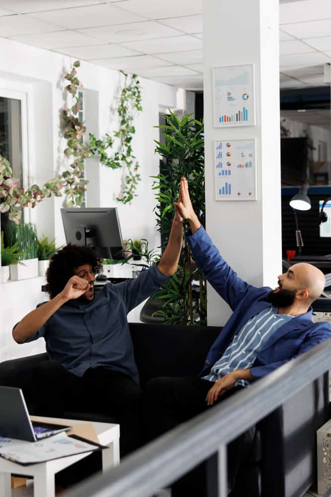 excited people giving high-five while checking sales results having success with plants in office